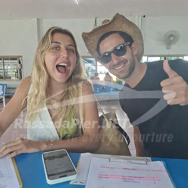 Two excited tourists smiling and giving a thumbs-up while checking in at the Rassada Pier ticket counter