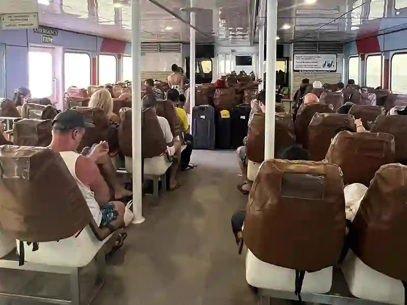 Interior cabin of a standard Phuket passenger ferry showing spacious air-conditioned seating, wide aisles, and large luggage storage areas.